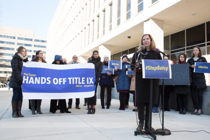 Stacy Malone speaks at a press conference in front of a banner that says "Hands Off Title IX."