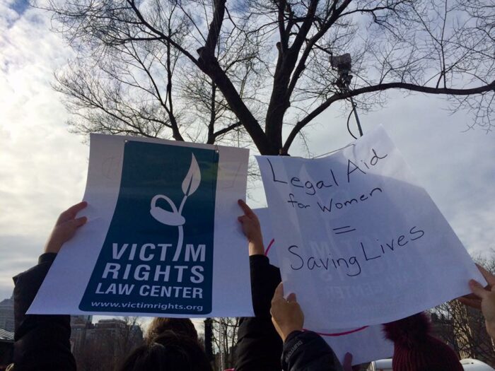 VRLC Staff hold up signs at the 2017 Women's March with the VRLC logo that read "Legal Aid for Women = Saving Lives"
