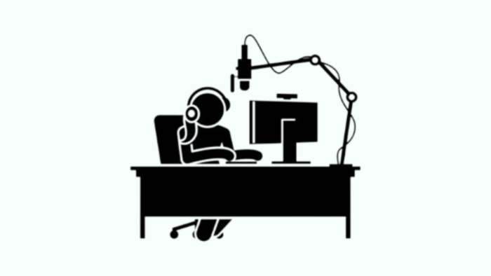 A person sitting at a desk with a microphone and computer, recording a podcast.