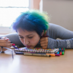 A sad person with their chin resting on a notebook on a desk.