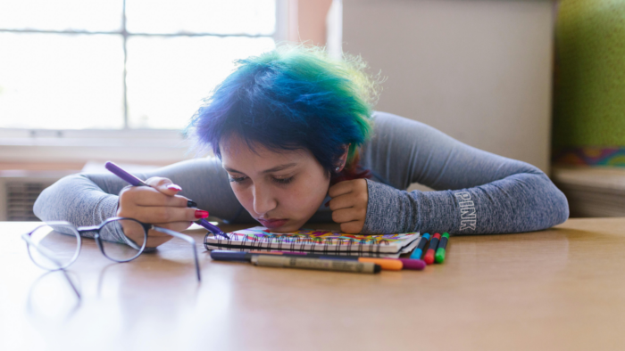 A sad person with their chin resting on a notebook on a desk.